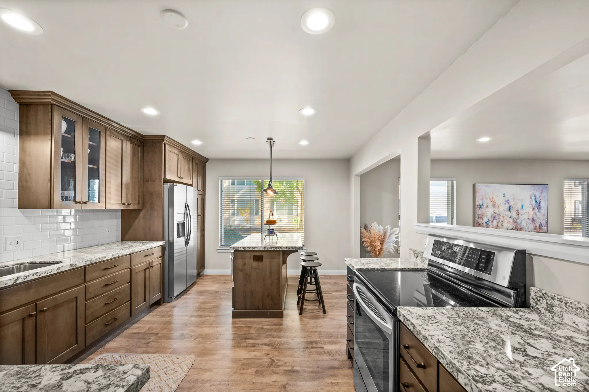 Kitchen featuring wood-finish cabinetry, stone-patterned countertops, a center island with pendant lighting, stainless steel appliances, and wood-finish flooring