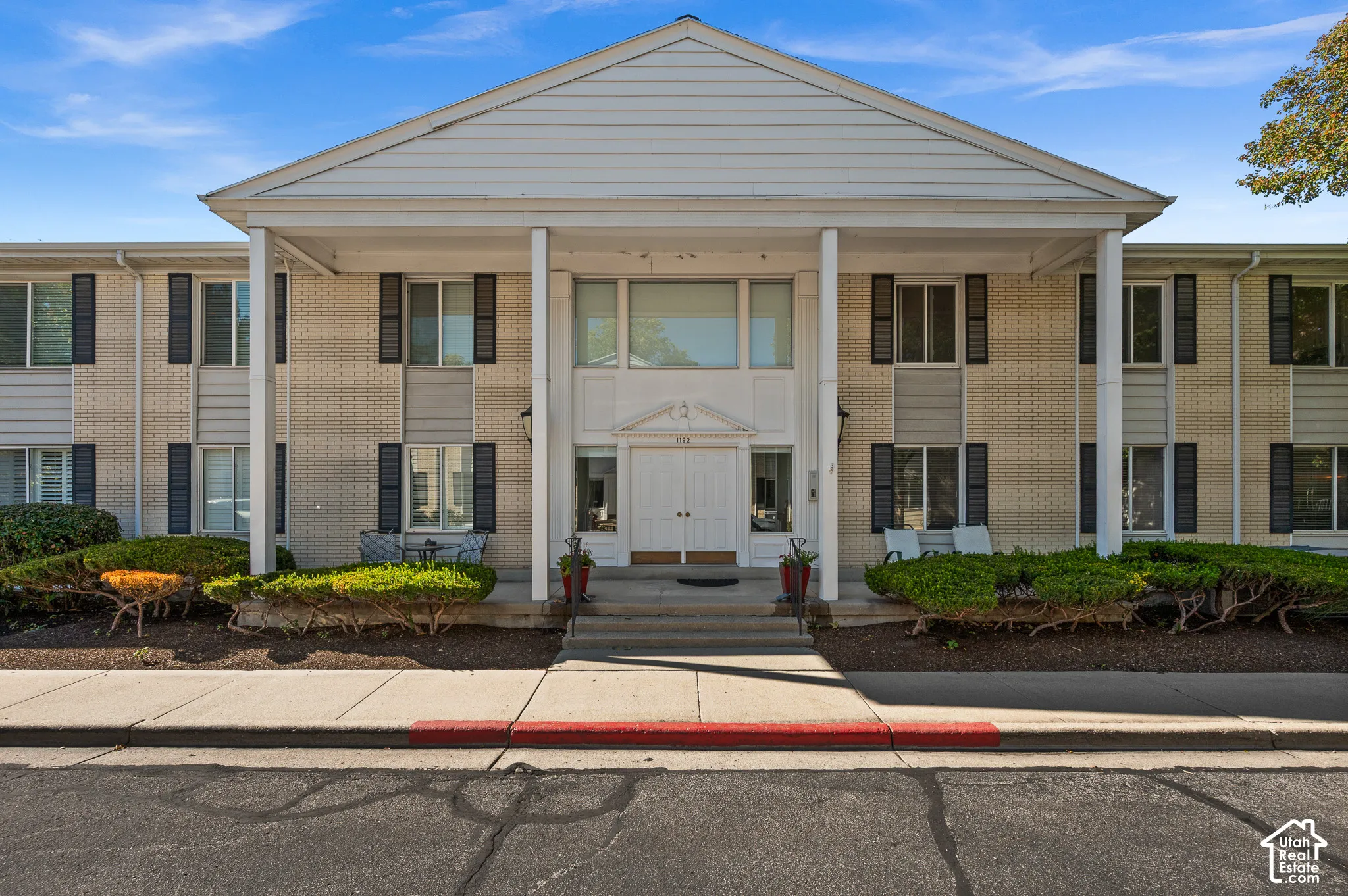 Colonial-style facade featuring light brick masonry, a covered portico with square columns, dual-pane windows with dark shutters, and a pedimented entryway with double doors