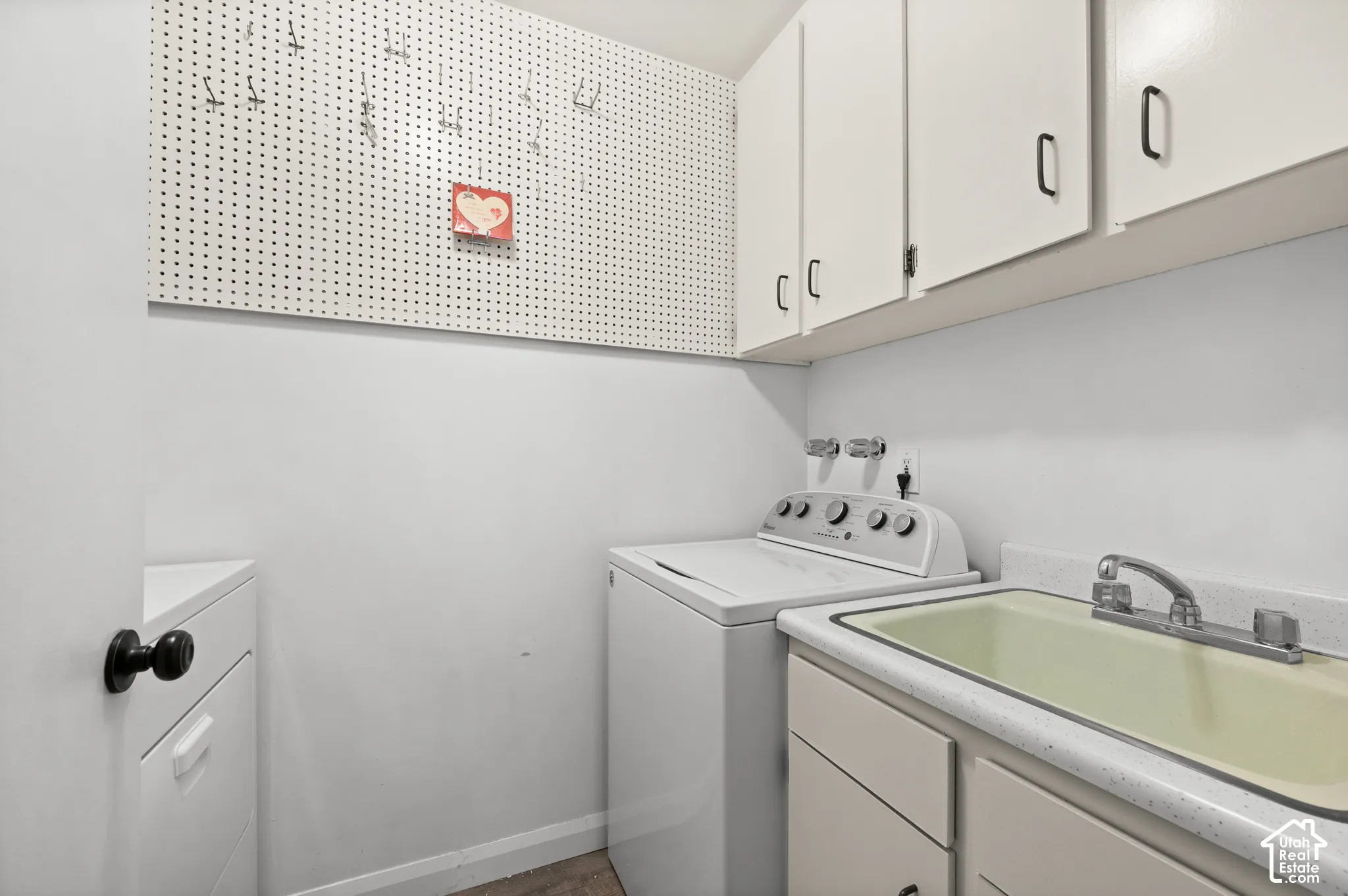 Utility space featuring overhead wall-mounted cabinets, integrated pegboard wall storage, a drop-in sink, and solid-surface countertop