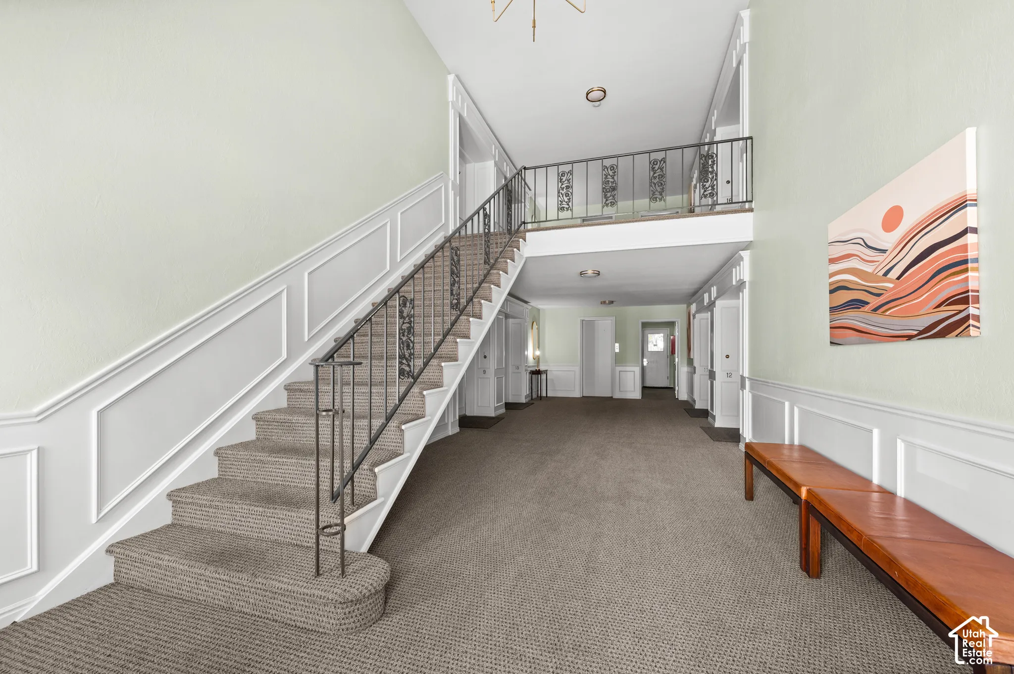 Foyer featuring wall molding, a staircase with metal railings, a mezzanine landing, and neutral carpeting