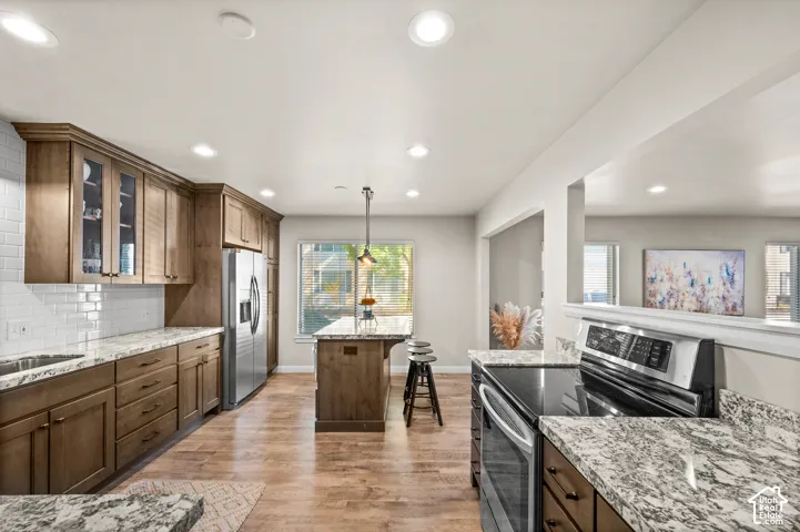 Kitchen featuring wood-finish cabinetry, stone-patterned countertops, a center island with pendant lighting, stainless steel appliances, and wood-finish flooring