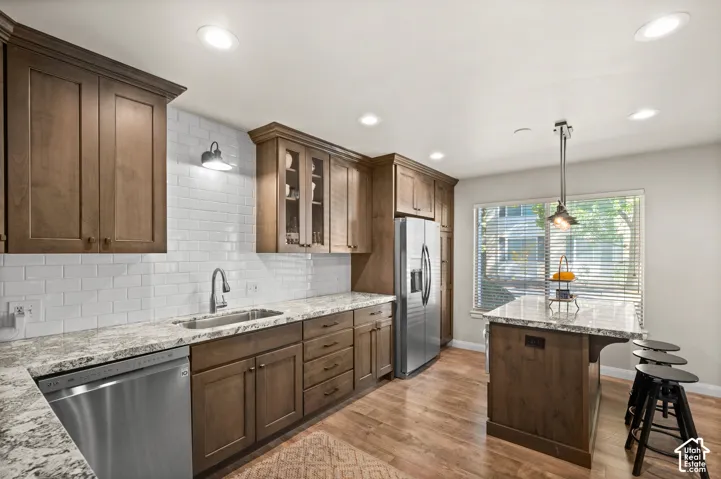 Kitchen featuring wood cabinetry, stone-surface countertops, subway tile backsplash, stainless steel appliances, and a central island