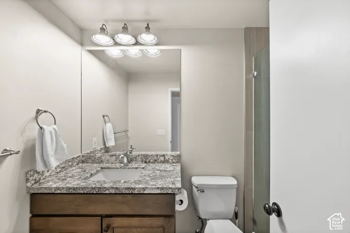 Bathroom featuring wood-finish cabinetry, stone-patterned countertop with an integrated basin, triple-light vanity fixture, large wall-mounted mirror, and glass-enclosed shower