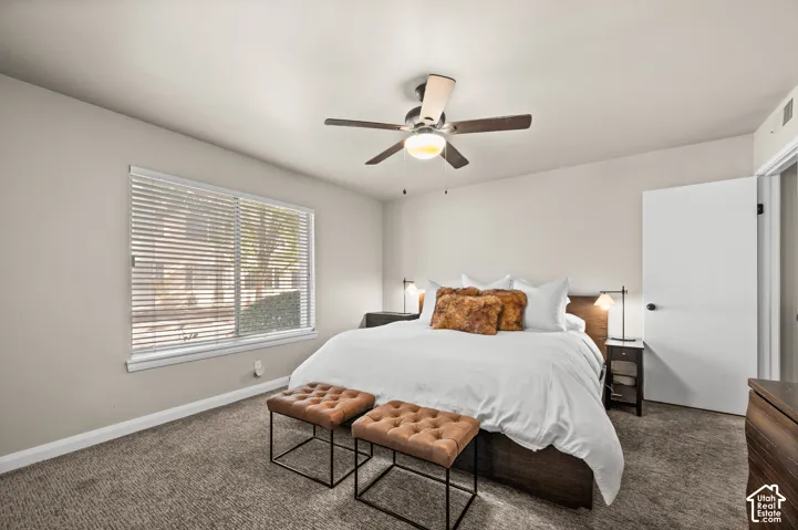 Neutral wall color, carpeted flooring, window with horizontal blinds, and a ceiling-mounted light fixture with a fan