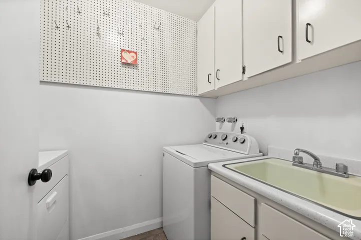 Utility space featuring overhead wall-mounted cabinets, integrated pegboard wall storage, a drop-in sink, and solid-surface countertop