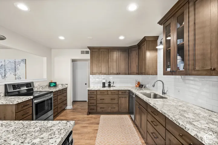 Kitchen featuring stained wood cabinetry, stone-surface countertops, white subway tile backsplash, recessed lighting, and stainless steel appliances