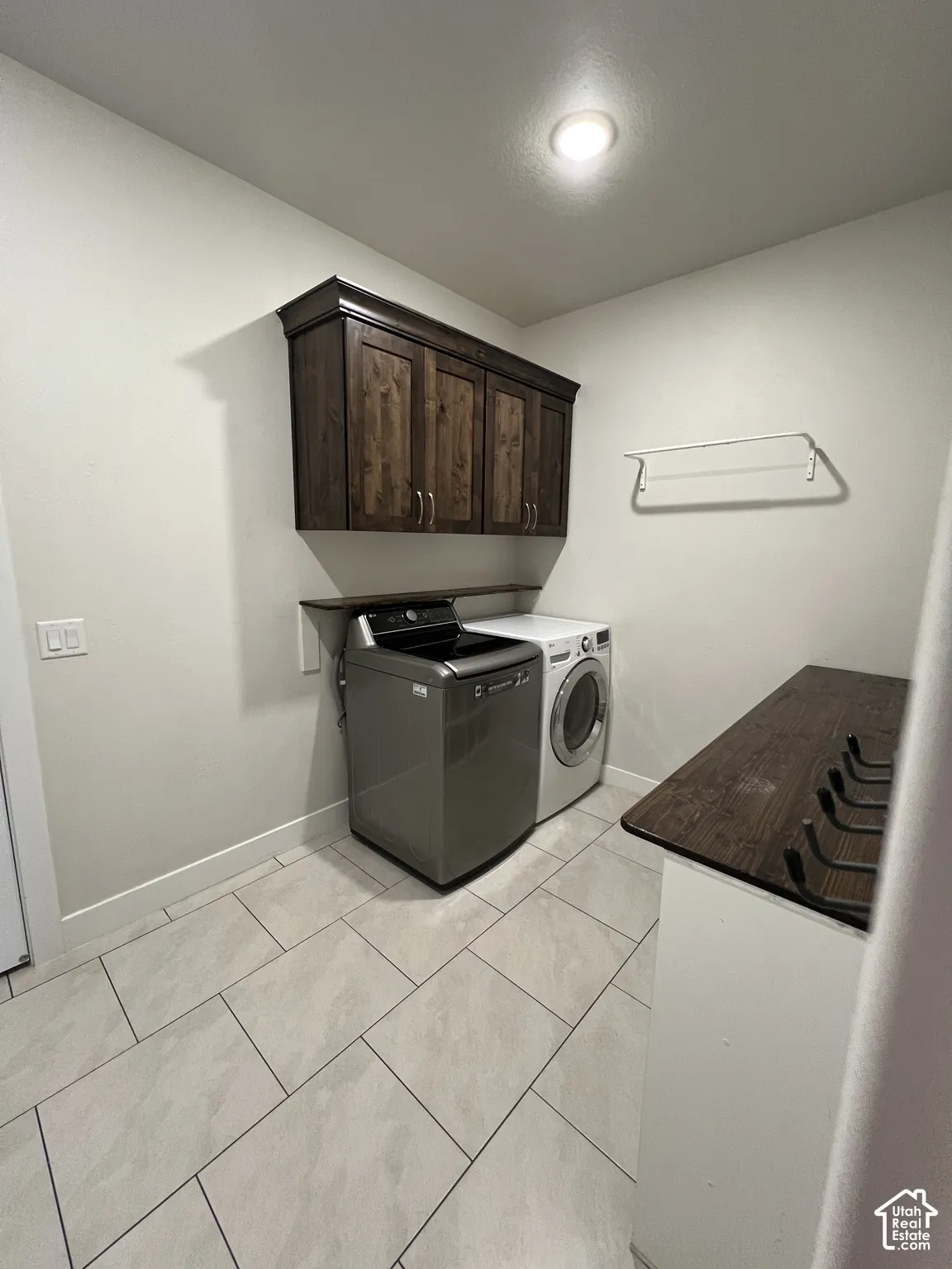 Laundry room featuring large-format tile flooring, stained wood-finish wall cabinetry, a built-in wood-finish counter surface with hooks, and a wall-mounted drying rack