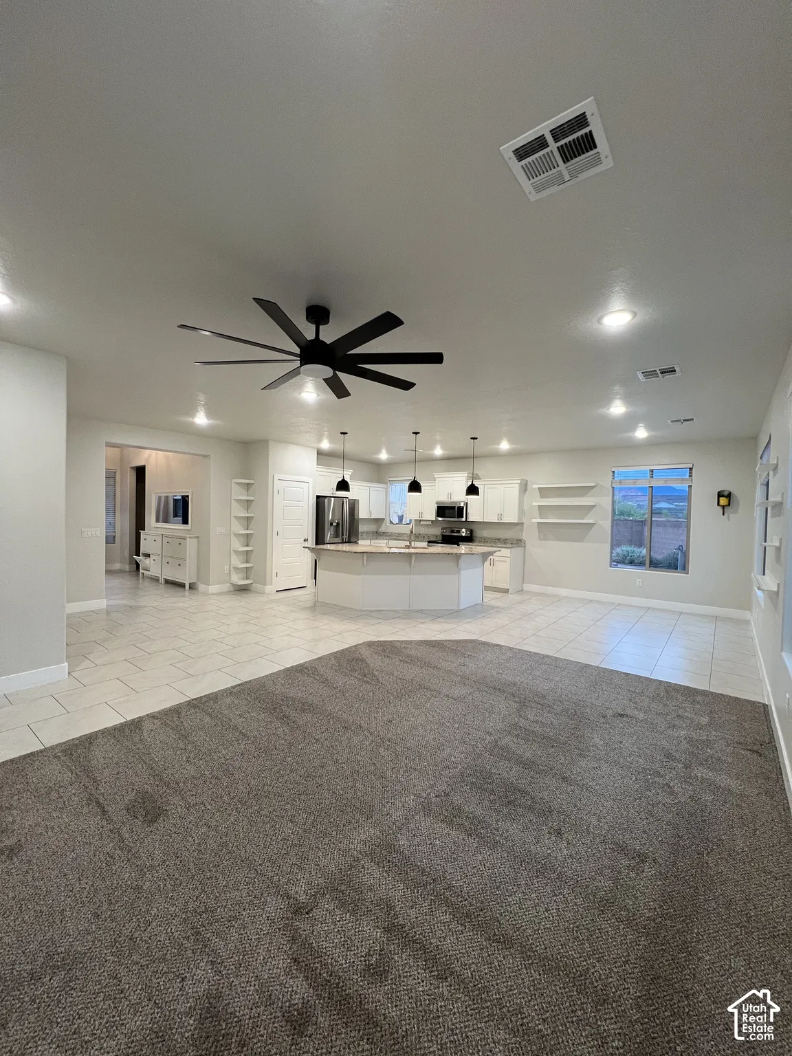 Open-concept interior featuring a spacious kitchen with a central island, white cabinetry, tile flooring, and integrated recessed lighting