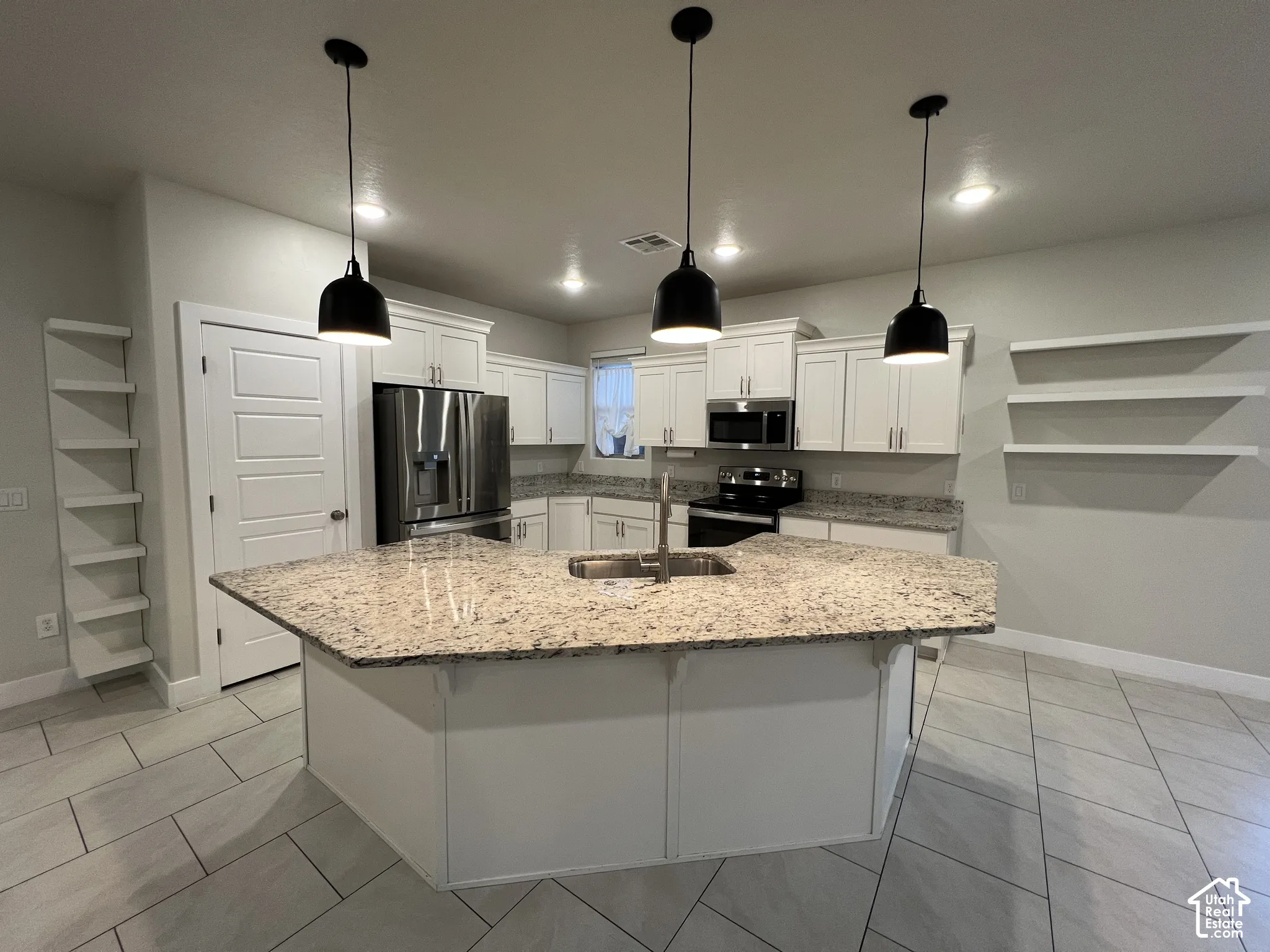 Kitchen featuring white cabinetry, stone countertops, stainless steel appliances, tiered open shelving, and three pendant lights over a central island