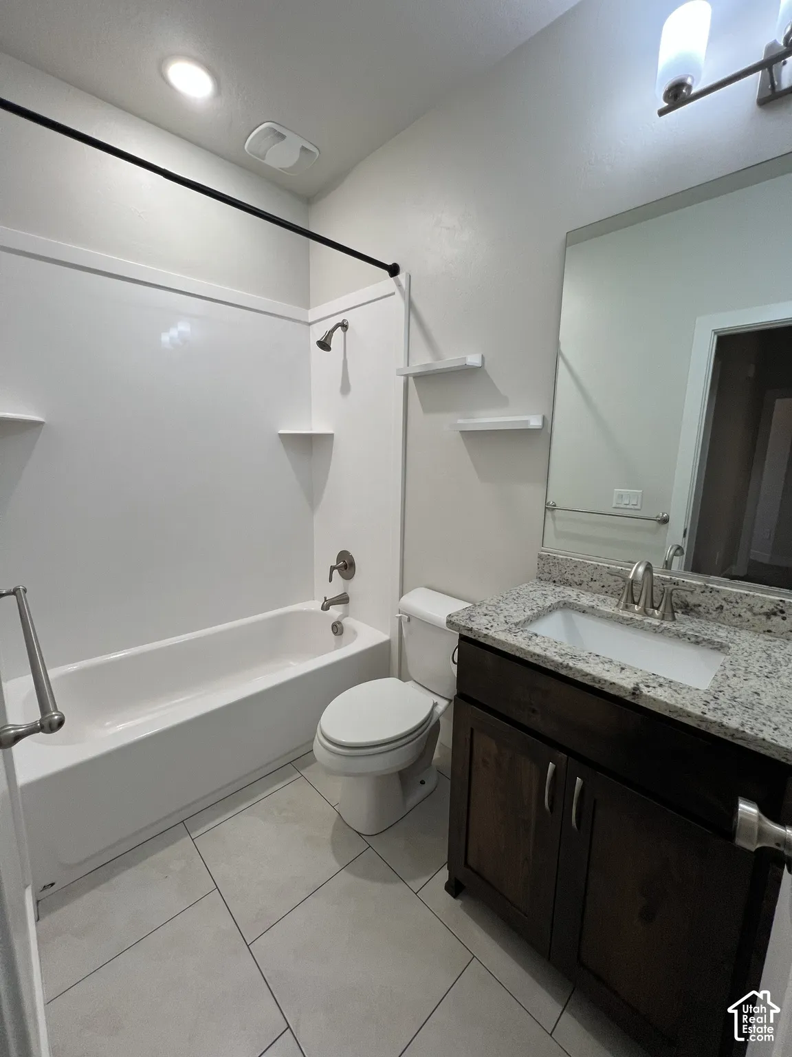 Bathroom featuring a dark wood-finish vanity, stone-patterned countertop with an integrated rectangular sink, large wall-mounted mirror, and tile flooring