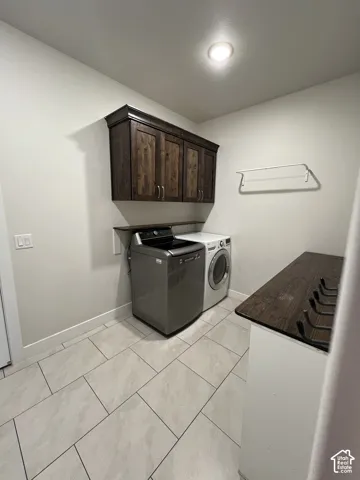 Laundry room featuring large-format tile flooring, stained wood-finish wall cabinetry, a built-in wood-finish counter surface with hooks, and a wall-mounted drying rack