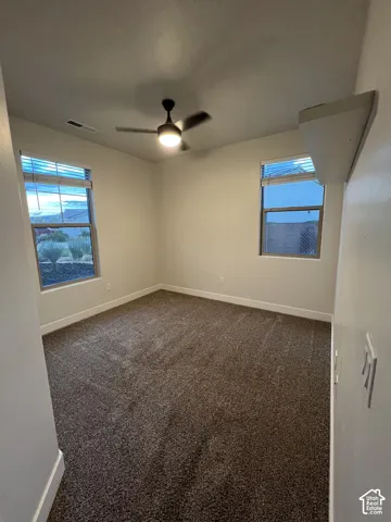 Neutral interior featuring wall-to-wall carpeting, dual windows with horizontal blinds, and a central ceiling fan with an integrated light fixture