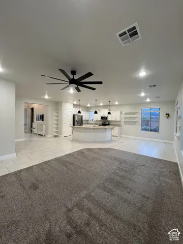 Open-concept interior featuring a spacious kitchen with a central island, white cabinetry, tile flooring, and integrated recessed lighting