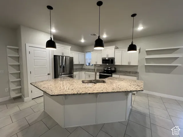 Kitchen featuring white cabinetry, stone countertops, stainless steel appliances, tiered open shelving, and three pendant lights over a central island