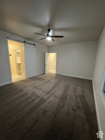 Neutral-toned carpeted flooring, sliding barn door, and a multi-blade ceiling fan with integrated lighting