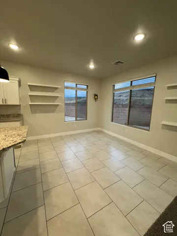Large-format tile flooring, stone-surfaced island countertop, recessed ceiling lighting, and built-in wall shelving