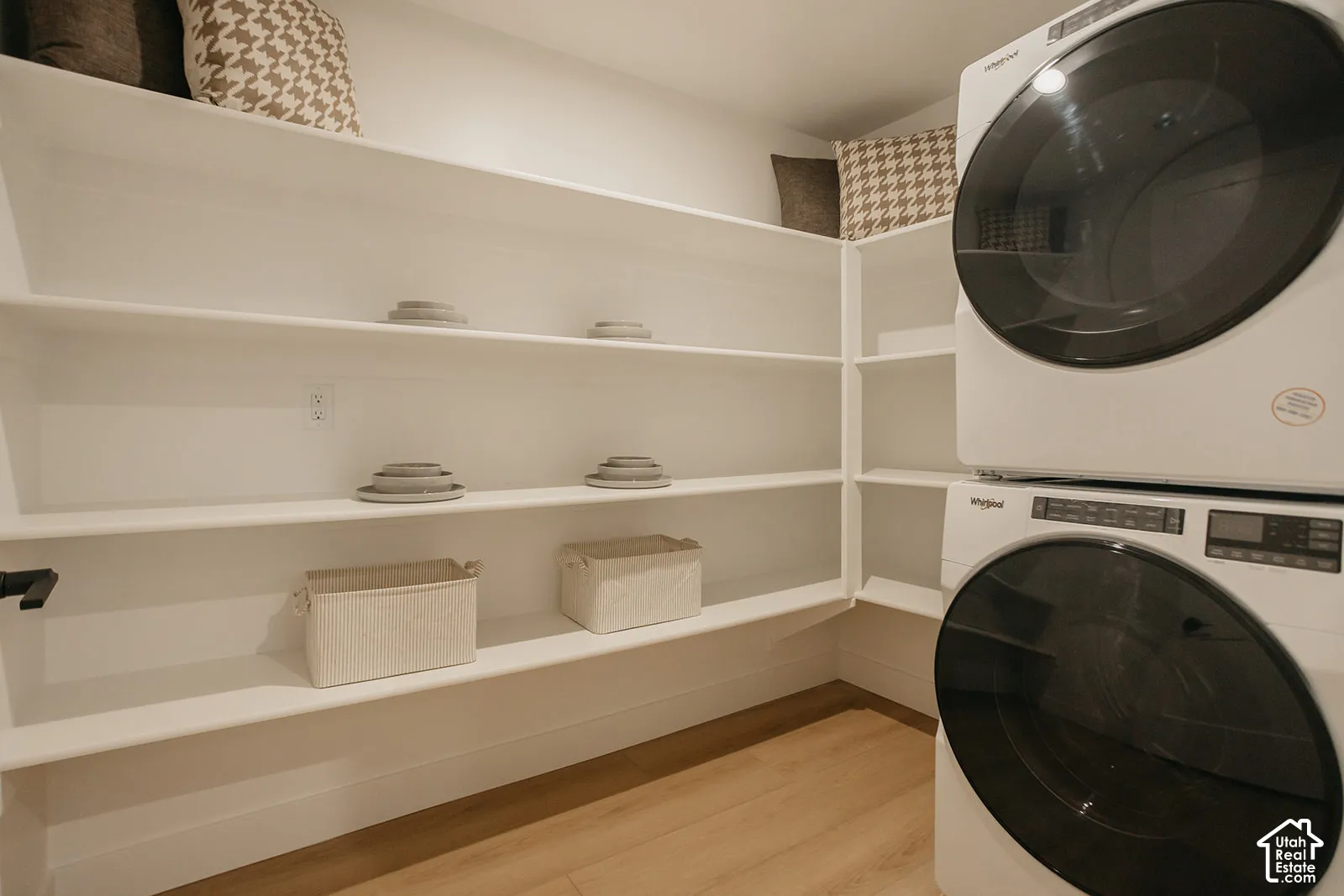 Laundry space featuring stacked front-load appliances and extensive built-in white shelving over wood-finish flooring