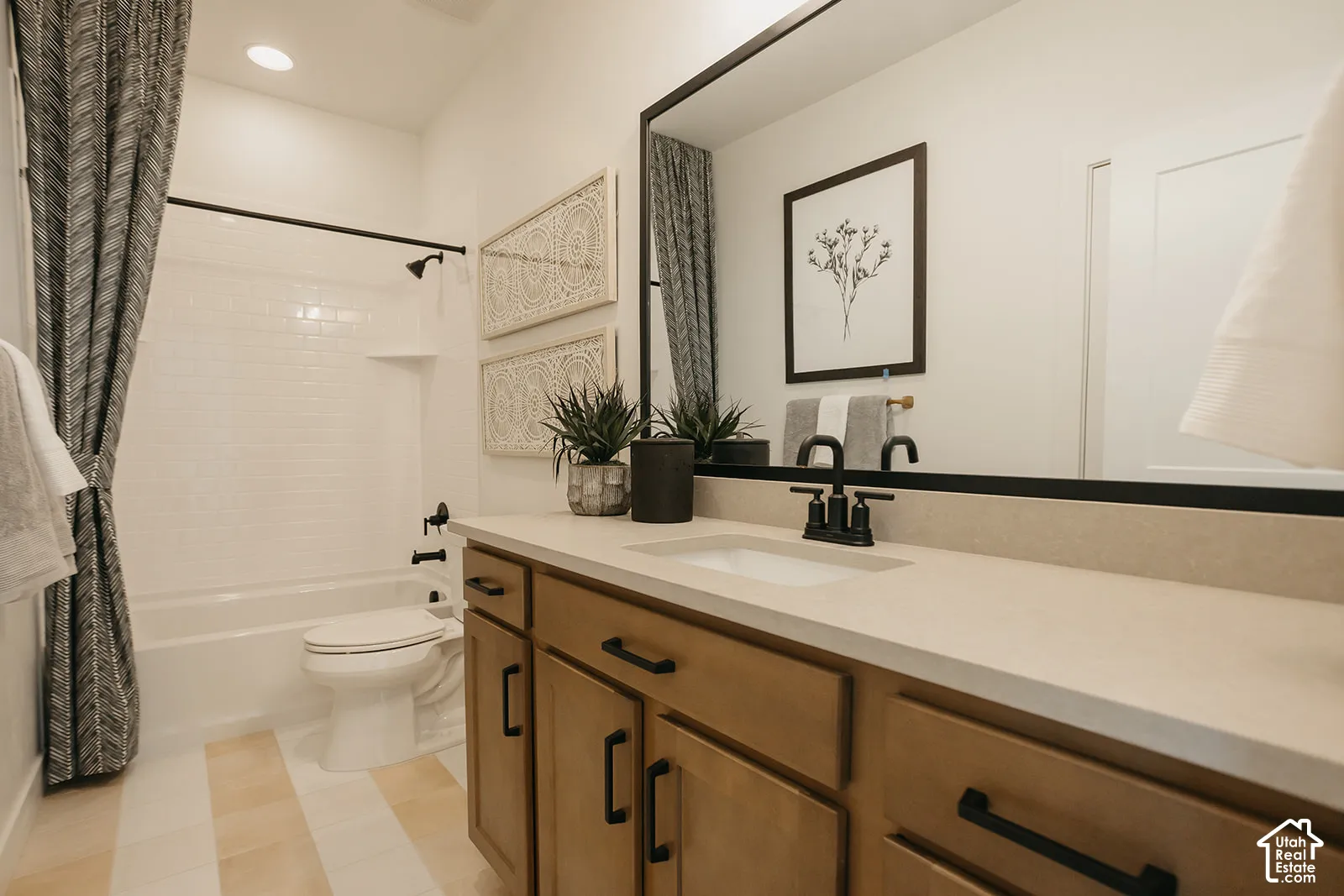 Bathroom vanity with stone-composite countertop, undermount sink, and matte black faucet, featuring a large-format framed mirror, shaker-style cabinetry with matte black hardware, and a tub-shower combination with white wall tile