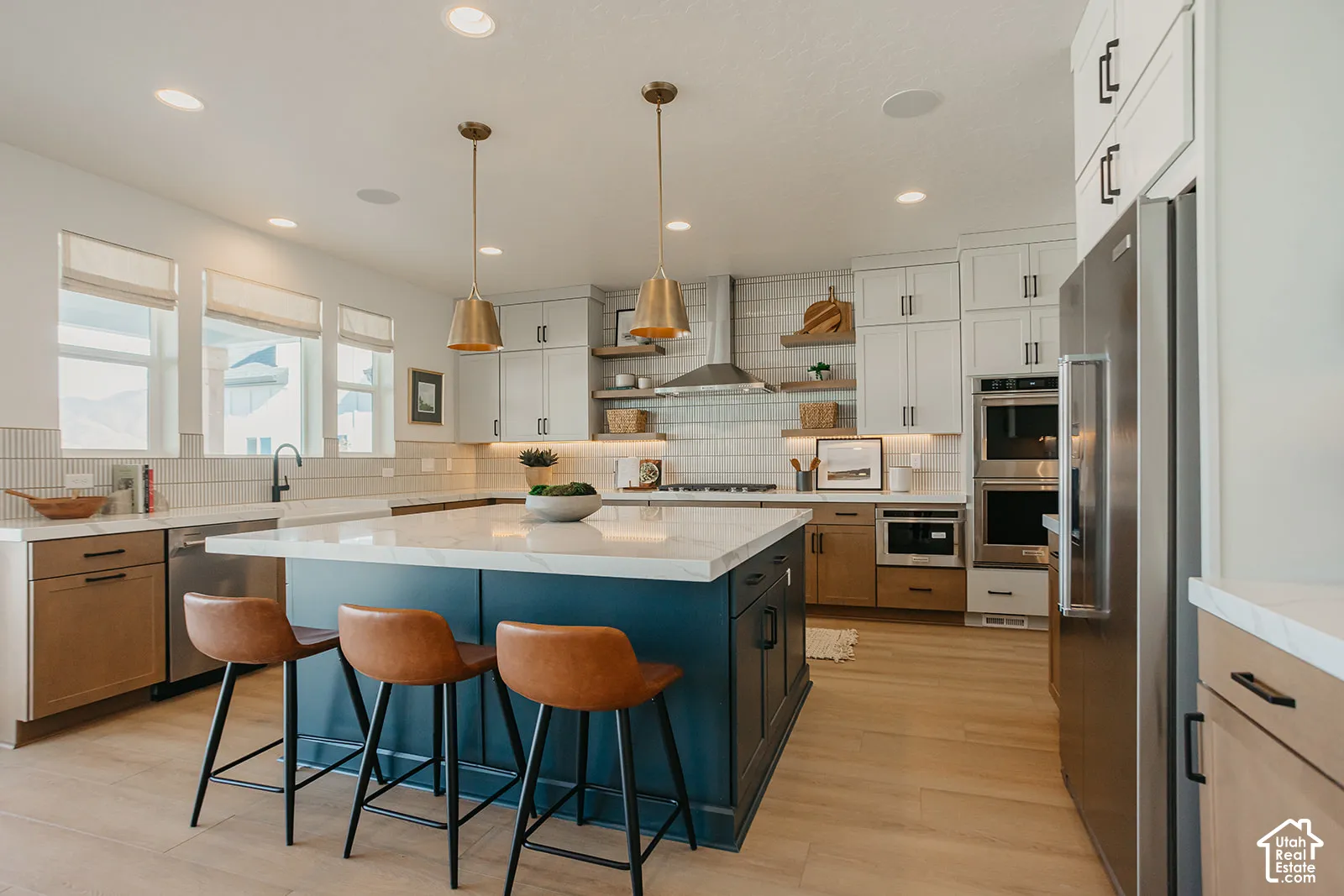 Kitchen featuring a central island with a contrasting navy finish, quartz countertops, two-tone cabinetry, wood-finish flooring, and stainless steel built-in appliances