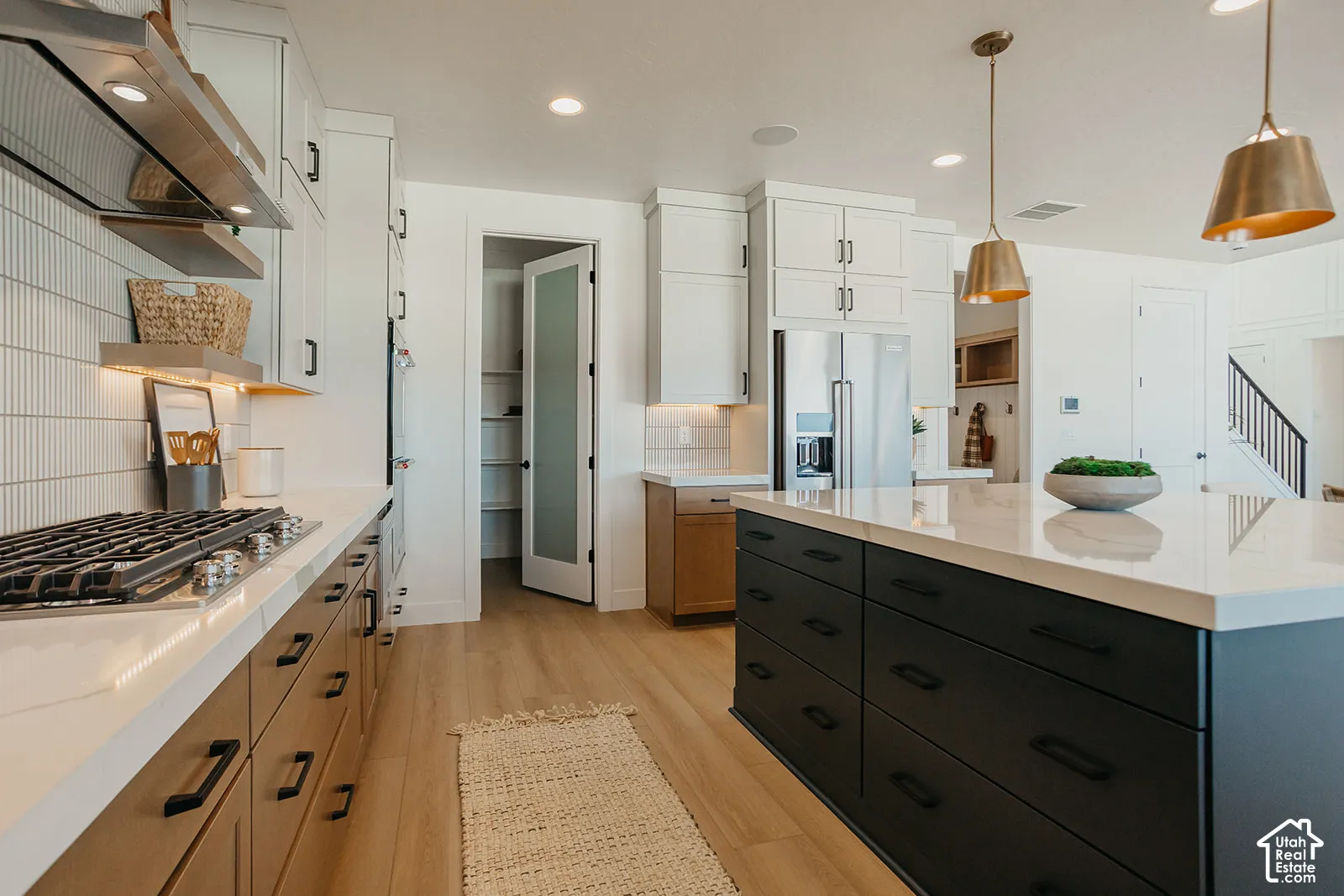 Kitchen featuring an expansive center island with matte finish cabinetry, quartz countertops, wood-finish flooring, vertical tile backsplash, and stainless steel appliances