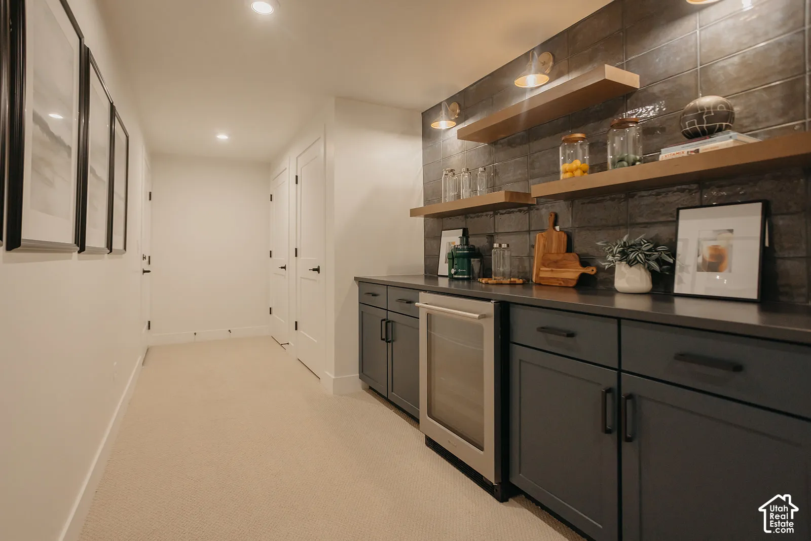 Wet bar featuring matte charcoal cabinetry, dark solid-surface countertops, textured tile backsplash, built-in stainless steel beverage refrigerator, and floating wood shelves