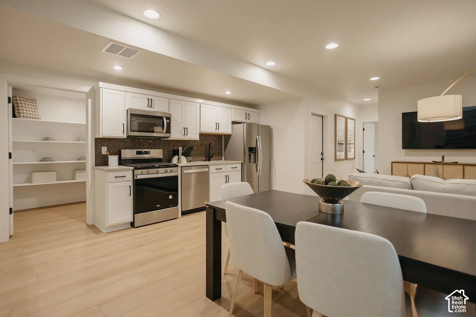 Kitchen featuring white shaker-style cabinetry, stainless steel appliances, wood-finish flooring, and a walk-in pantry with built-in shelving