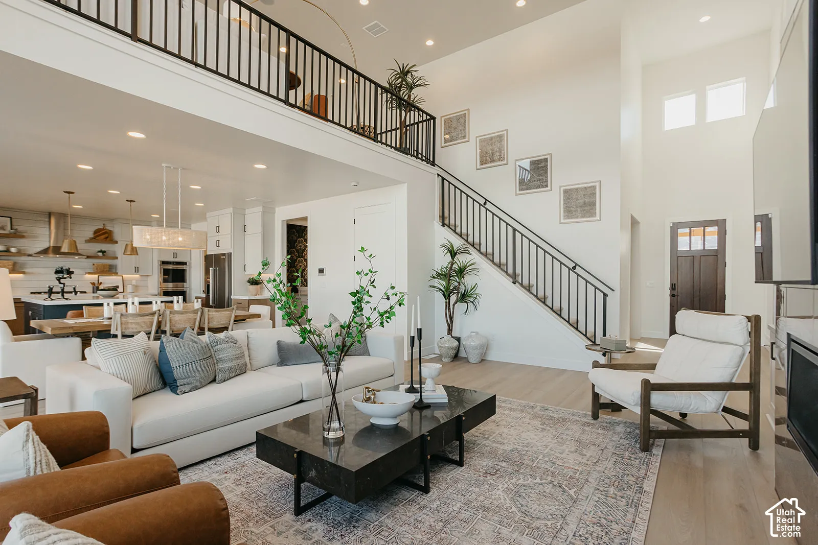 Open-concept living space featuring high ceilings, wood-finish flooring, recessed lighting, and a staircase with a metal railing