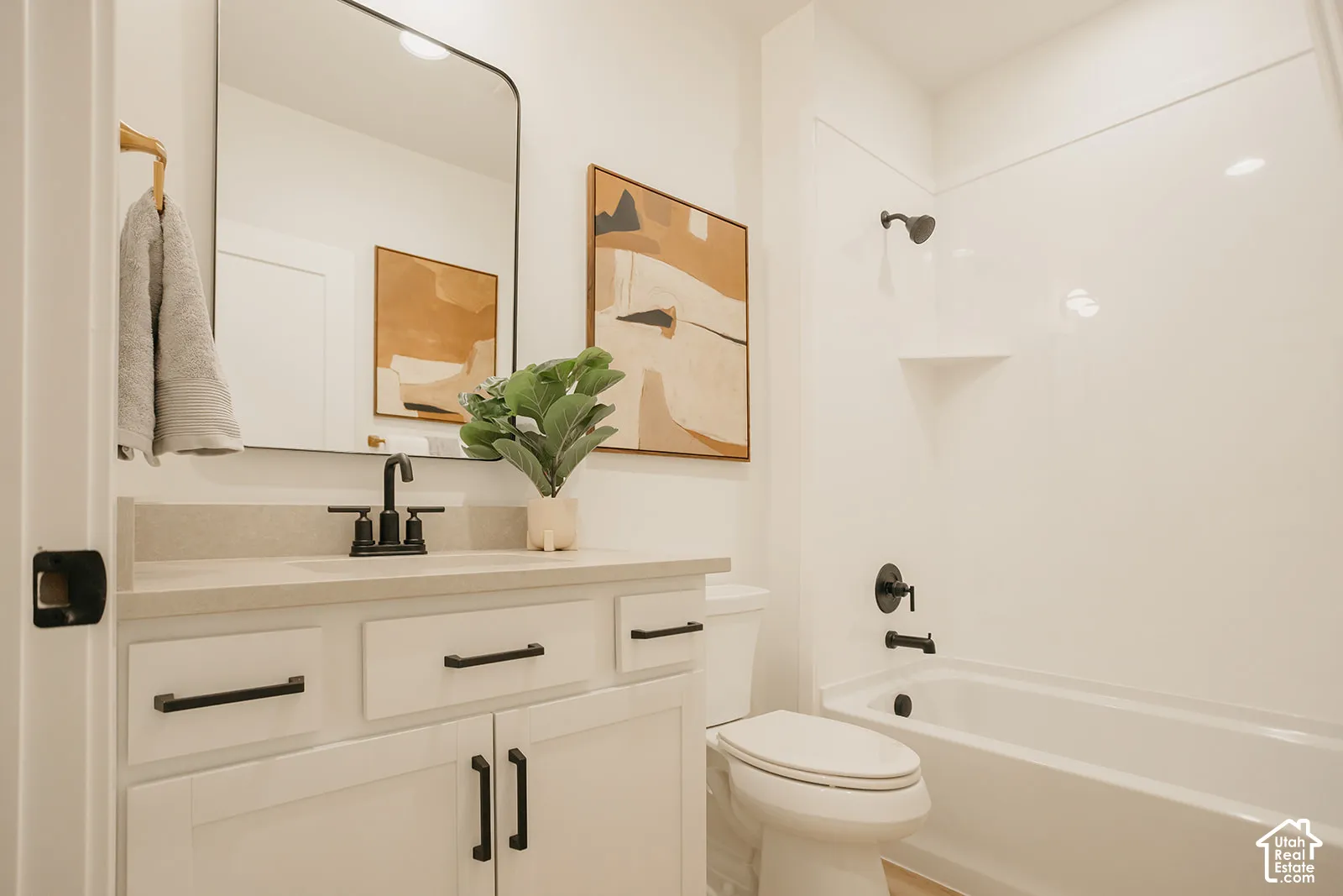 White vanity with a neutral solid-surface countertop, rectangular undermount sink, matte black hardware, and a matching rounded rectangular mirror, accompanied by a white tub-and-shower combination featuring matte black fixtures