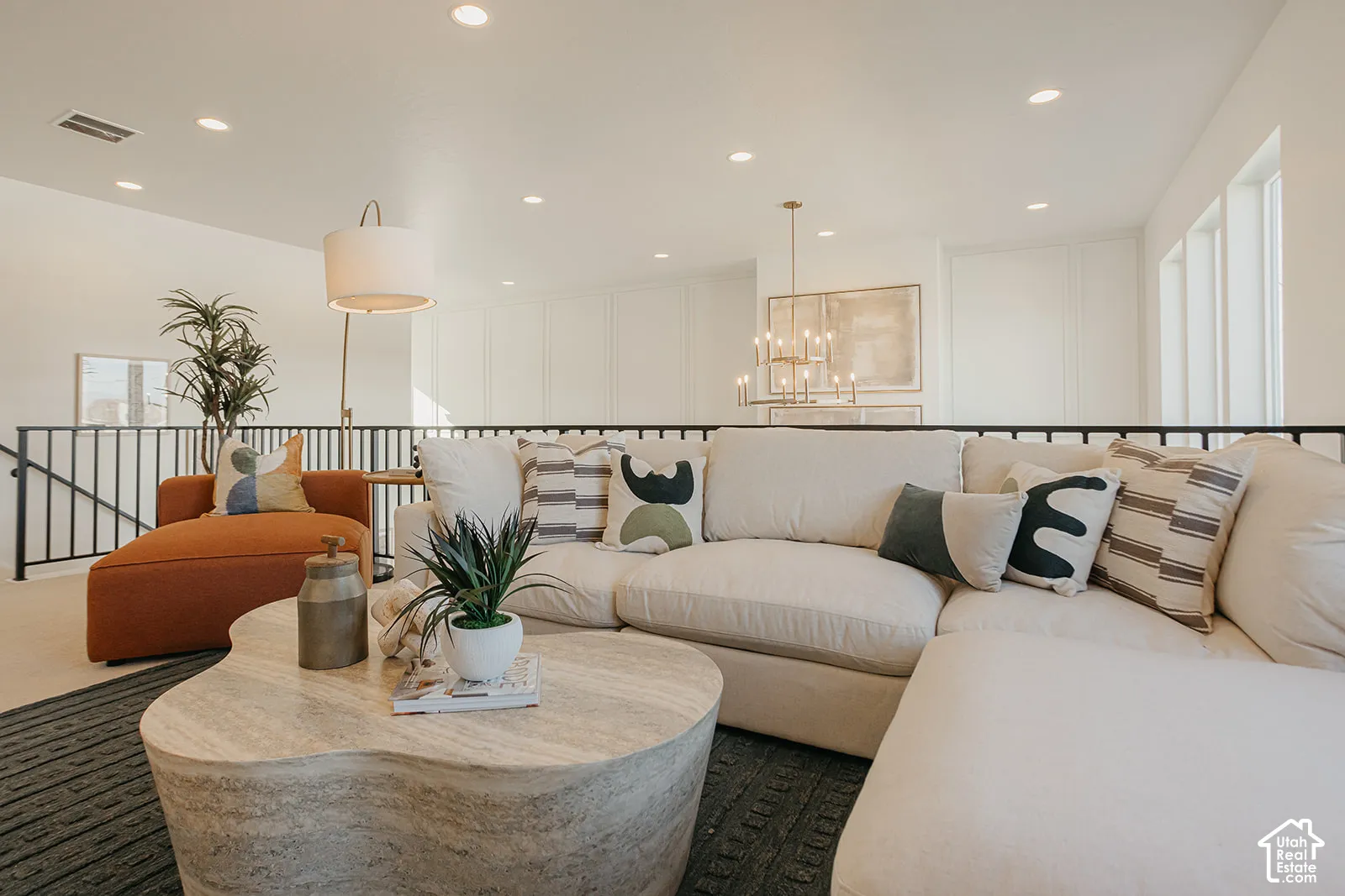 Living space featuring recessed lighting, paneled accent wall, metal railing, and multi-tier chandelier