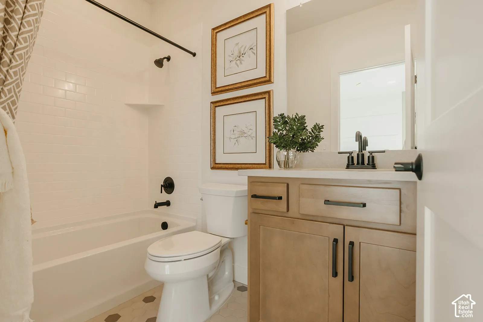 Bathroom featuring a vanity with light-tone wood cabinetry, a solid surface countertop, matte black hardware, a subway tile shower surround, and hexagonal floor tile