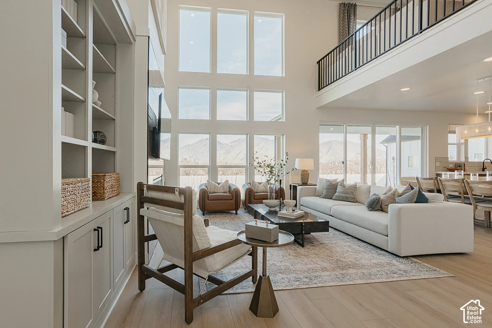 Double-height living area featuring floor-to-ceiling windows, built-in cabinetry, mountain scenery, and a mezzanine with metal railing