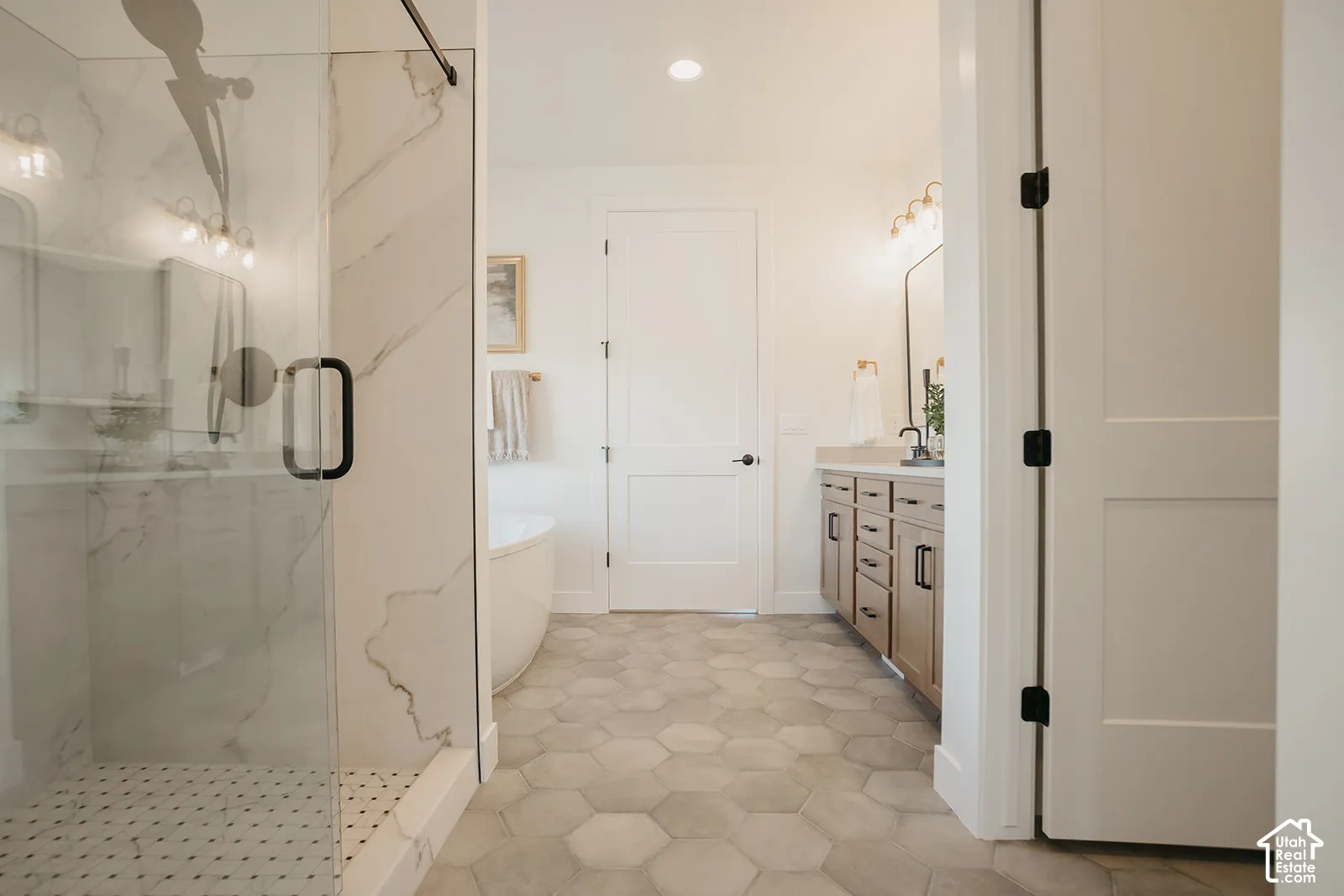 Bathroom featuring a glass-enclosed shower with large-format tile surround, freestanding soaking tub, dual-sink vanity with wood-finish cabinetry, and hexagonal tile flooring