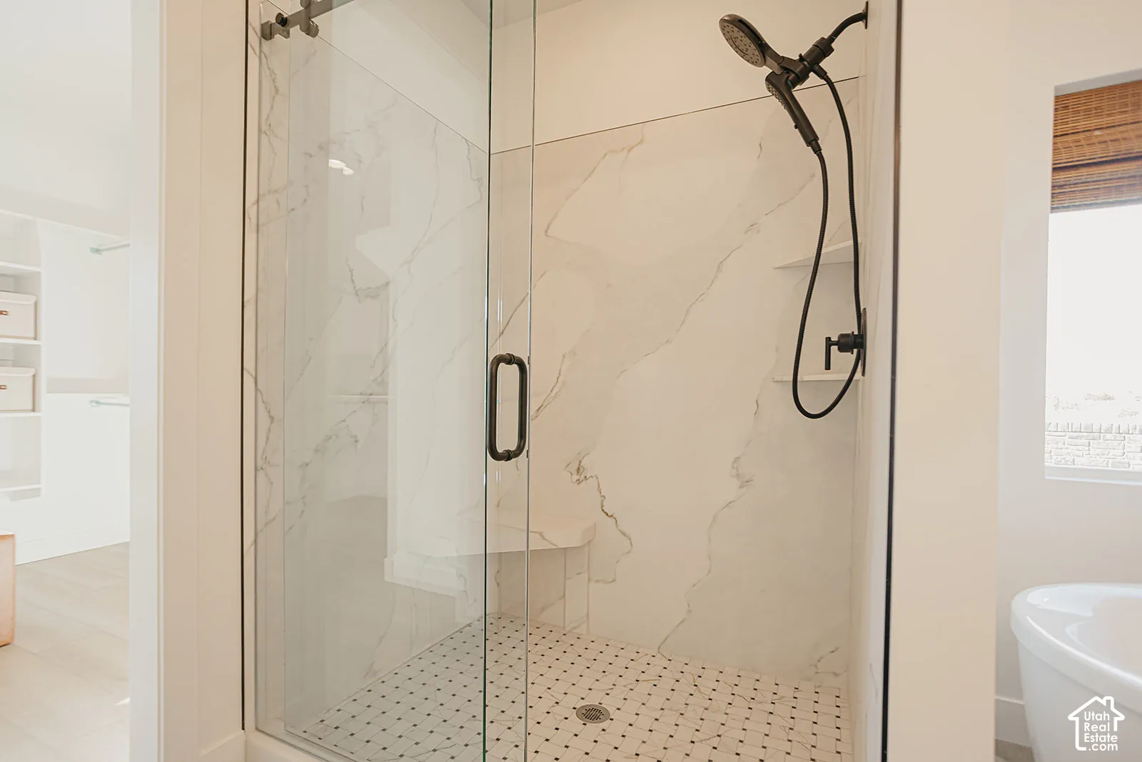 Walk-in shower featuring large-format wall tile, glass enclosure with matte black hardware, built-in bench, and a hand-held shower fixture