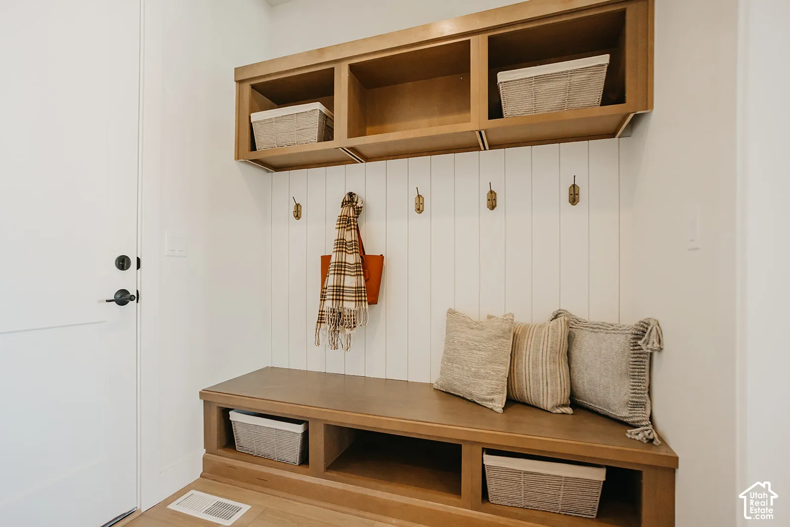 Built-in wood-finish cabinetry featuring open upper cubbies, lower storage compartments, and vertical shiplap wall paneling with mounted brass-tone hooks
