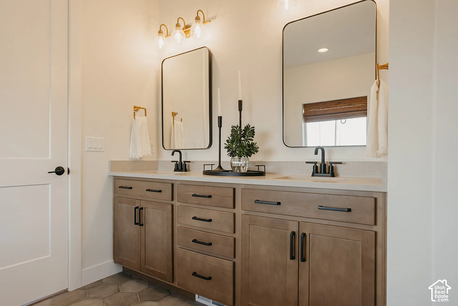 Double vanity featuring wood-finish cabinetry, matte black hardware, stone-surface countertops, dual rectangular under-mount sinks, and framed mirrors
