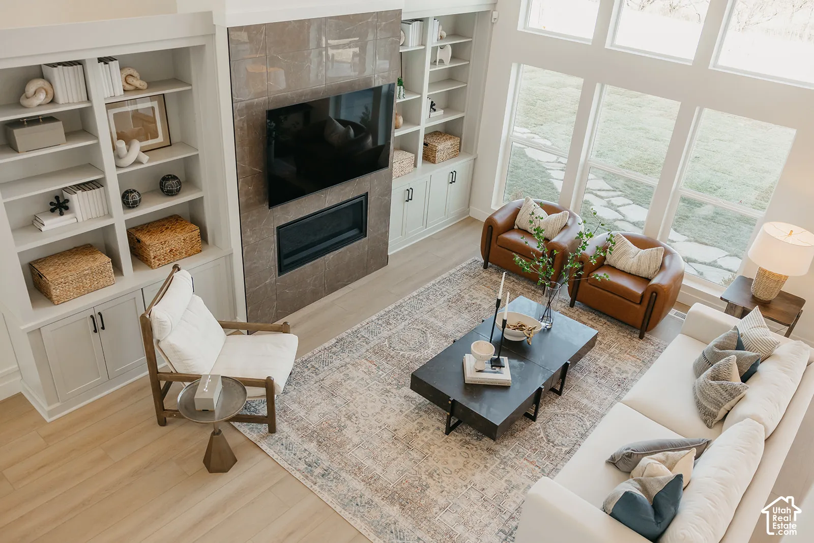 Living area featuring high ceilings, large windows, wood-finish flooring, a tile-surround fireplace, and custom built-in cabinetry