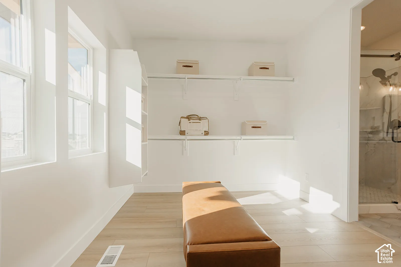 Walk-in closet featuring wood-finish flooring, built-in shelving, white wall-mounted storage racks, and natural lighting from large windows