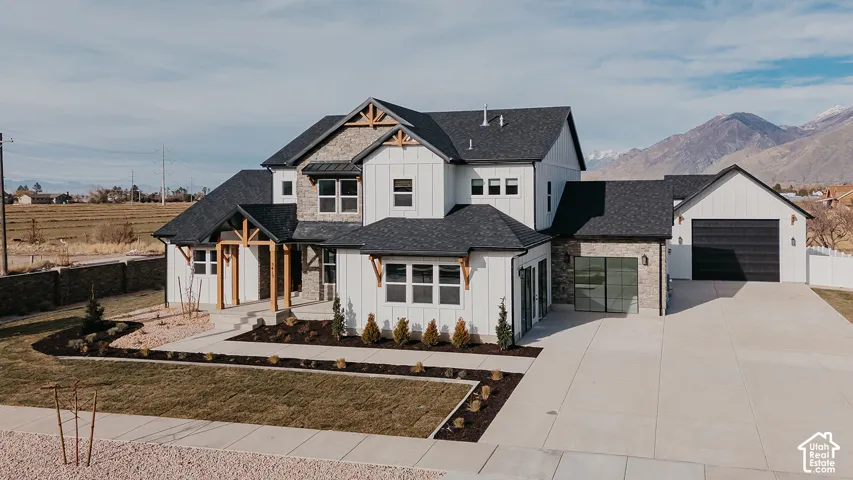 Exterior featuring white board-and-batten siding, natural stone accents, timber gable brackets, an attached garage, and a mountain backdrop