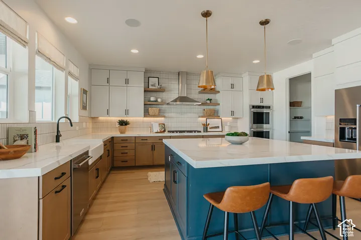 Kitchen featuring a large central island with a solid-surface countertop, custom cabinetry, farmhouse-style apron sink, built-in double wall ovens, and open wood shelving