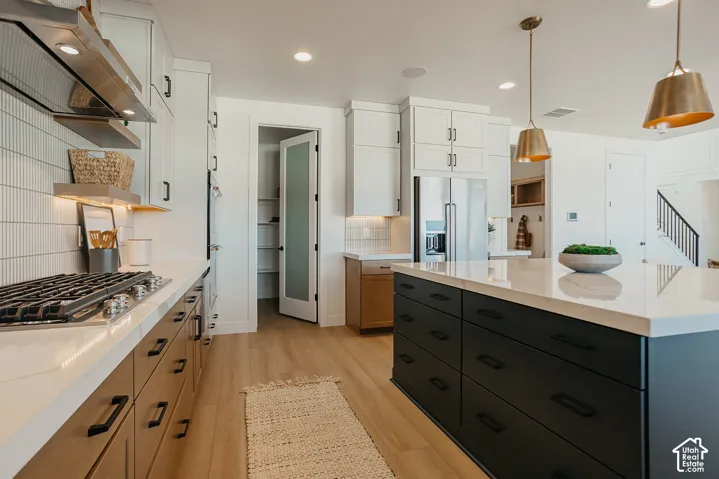 Kitchen featuring an expansive center island with matte finish cabinetry, quartz countertops, wood-finish flooring, vertical tile backsplash, and stainless steel appliances