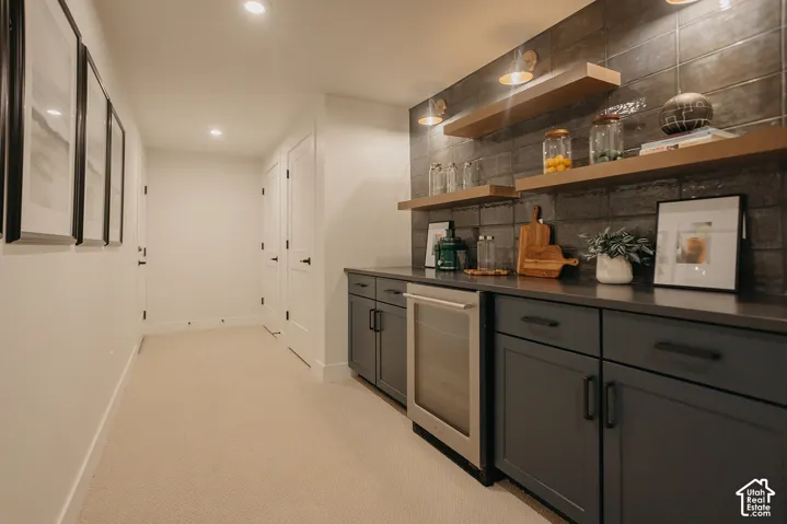 Wet bar featuring matte charcoal cabinetry, dark solid-surface countertops, textured tile backsplash, built-in stainless steel beverage refrigerator, and floating wood shelves
