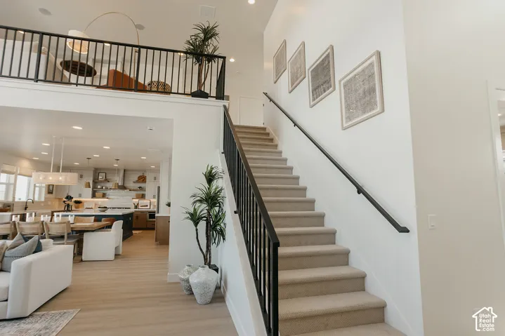 Two-story foyer featuring a carpeted staircase with a matte black metal railing, overhead recessed lighting, and wood-finish flooring