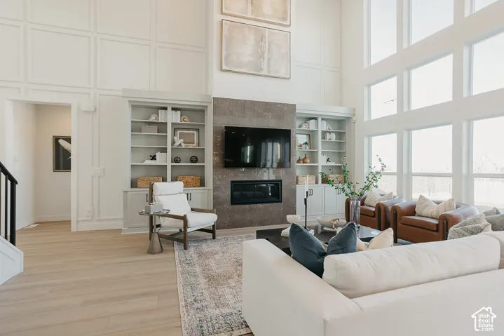 Double-height ceilings with floor-to-ceiling windows, custom built-in cabinetry, wood-finish flooring, and a fireplace with stone surround