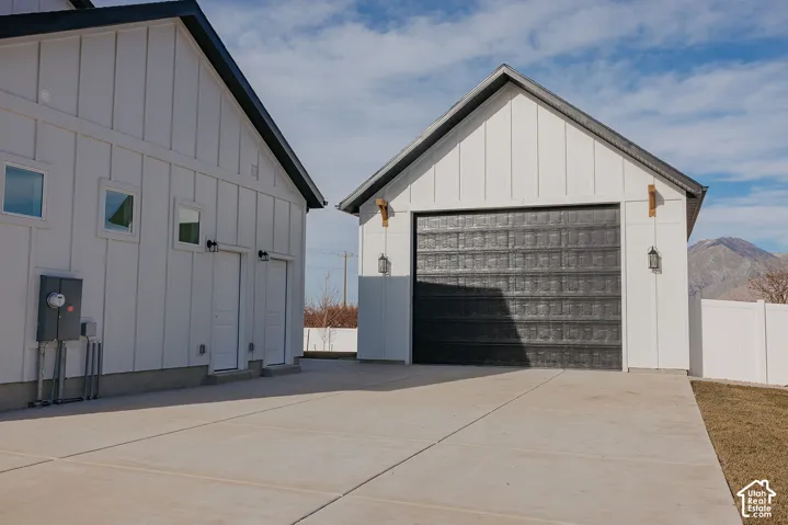Modern exterior featuring white vertical siding, a detached garage with a dark-finished door, concrete parking pad, and mountain backdrop