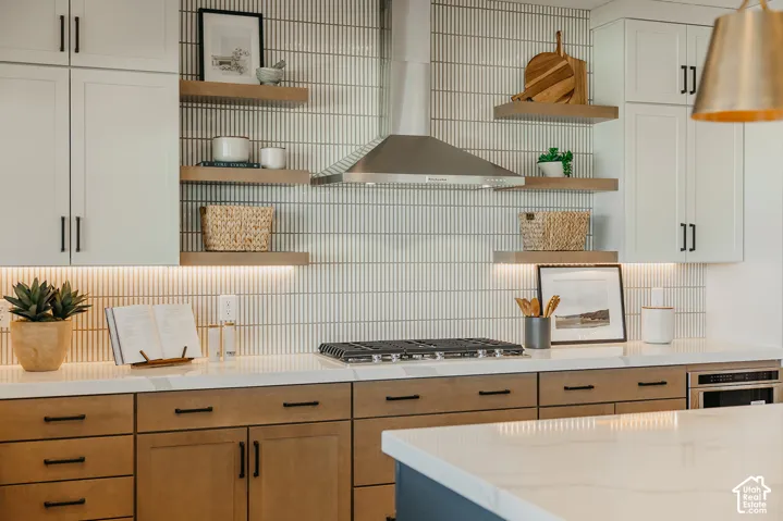 Kitchen featuring white shaker cabinetry, wood-finish lower cabinets, stone countertops, vertical tile backsplash, and stainless steel range hood