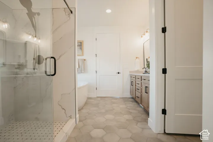Bathroom featuring a glass-enclosed shower with large-format tile surround, freestanding soaking tub, dual-sink vanity with wood-finish cabinetry, and hexagonal tile flooring