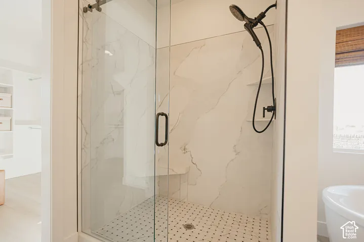 Walk-in shower featuring large-format wall tile, glass enclosure with matte black hardware, built-in bench, and a hand-held shower fixture