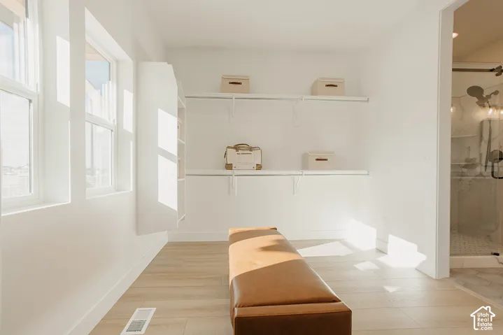 Walk-in closet featuring wood-finish flooring, built-in shelving, white wall-mounted storage racks, and natural lighting from large windows