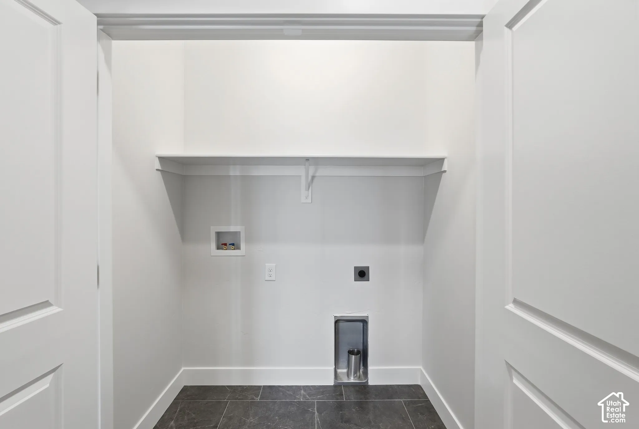 Dedicated laundry area featuring dual-panel entry doors, stone-finish tile flooring, built-in shelving, and integrated utility hookups