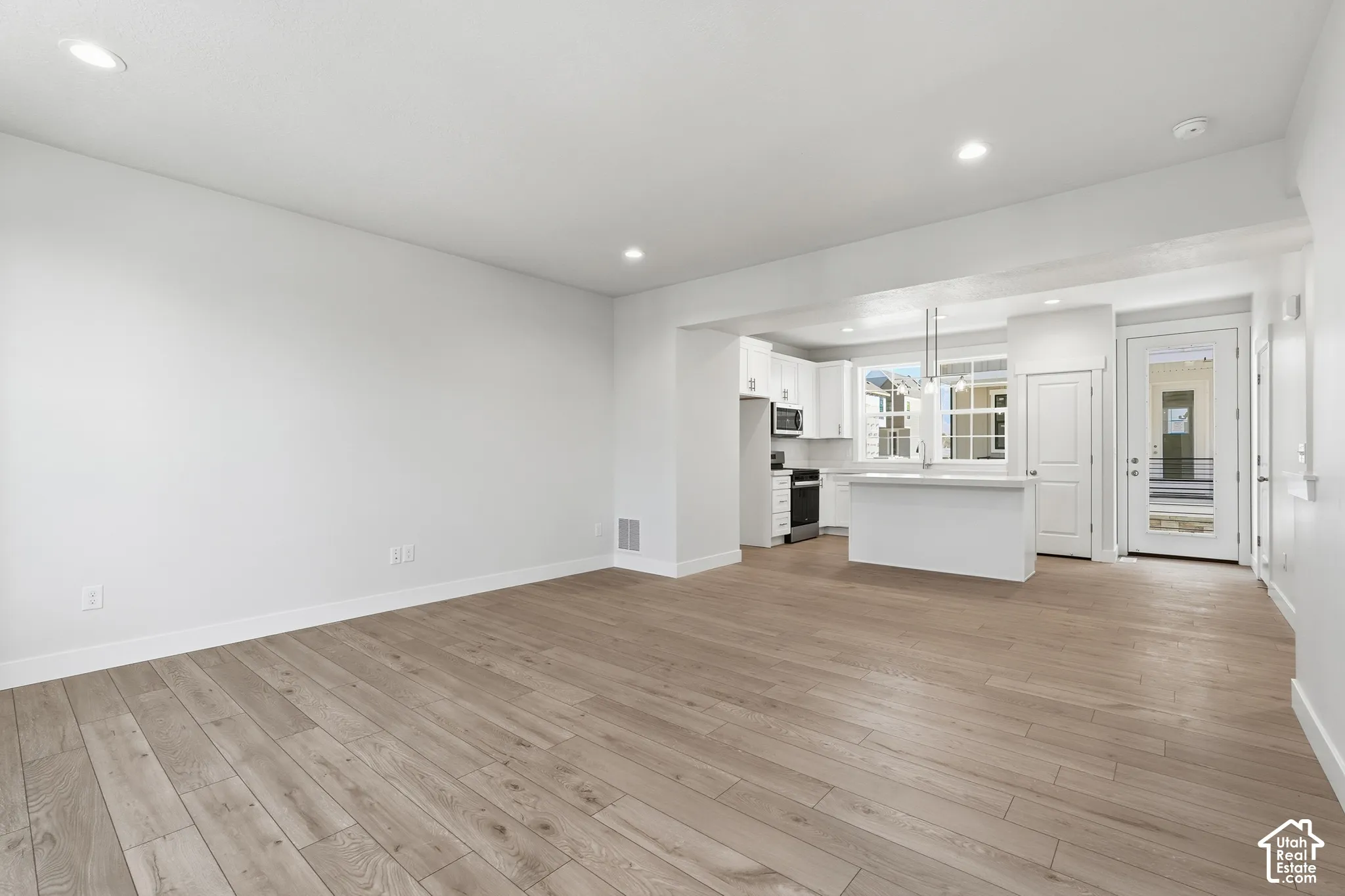Open-concept interior featuring light wood-finish flooring, recessed lighting, white cabinetry, a center island, and a glass-paneled exterior door